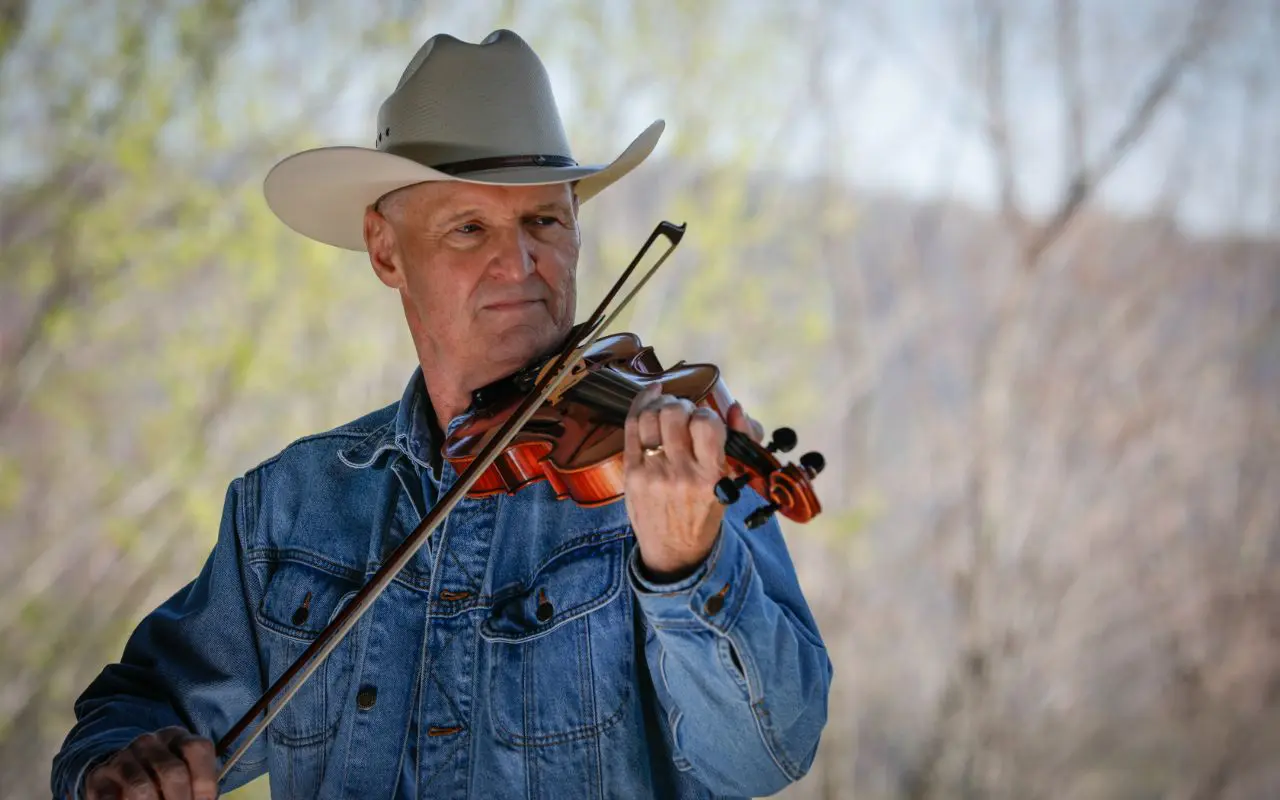 A man in cowboy hat playing violin outside.