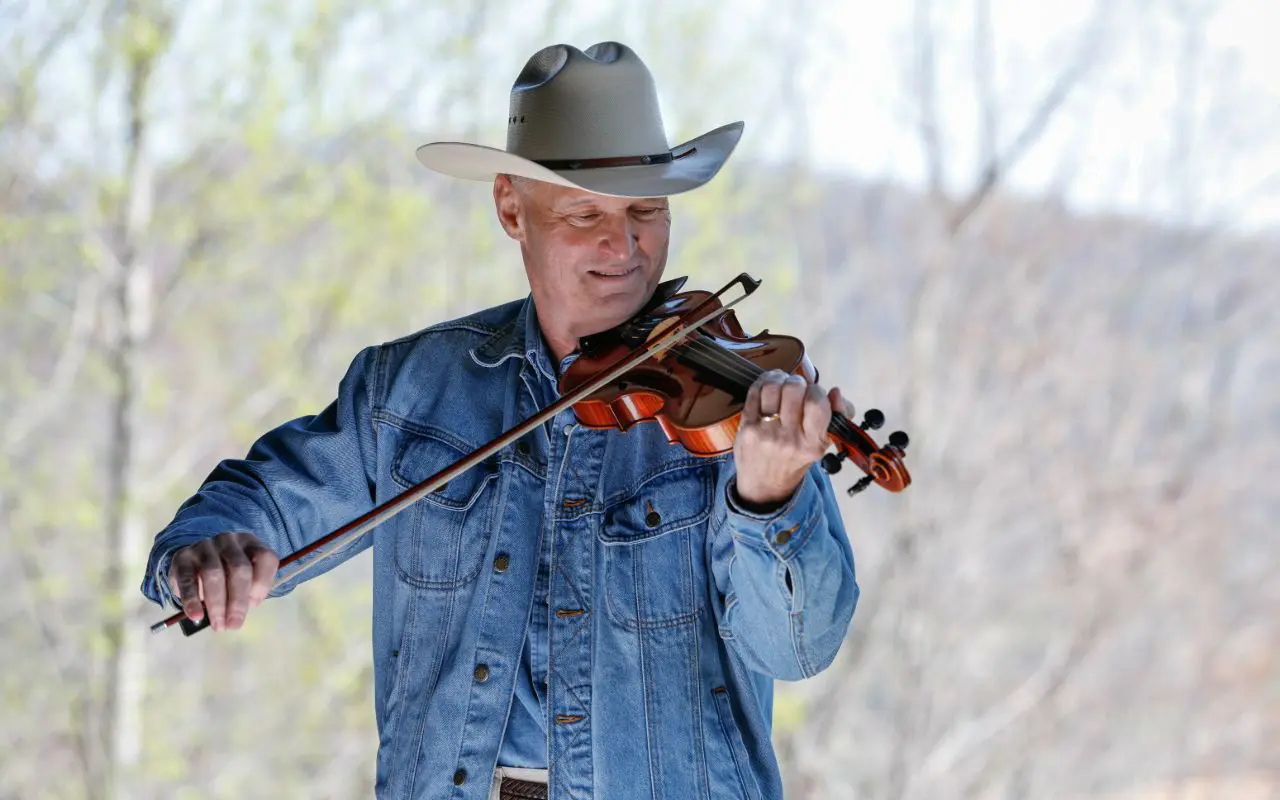 A man in cowboy hat playing violin outside.