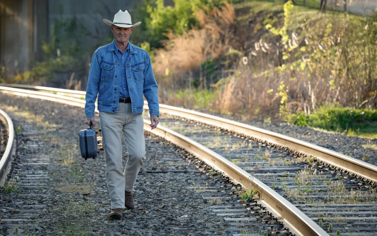 A man walking on the tracks with his suitcase.