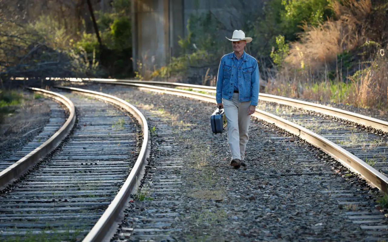 A man in cowboy hat walking on train tracks.